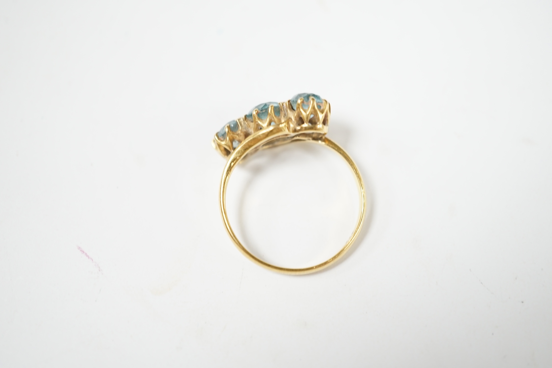 A yellow metal and three stone blue zircon set crossover ring, size L, gross weight 3 grams. Condition - poor
